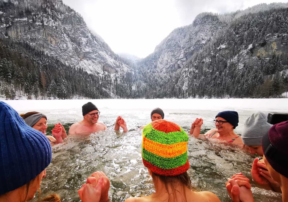 Retreatgruppe badet gemeinsam in einem Eisloch am verschneiten Gleinkersee
