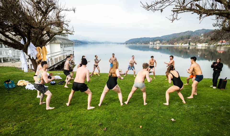 Gruppe bereitet sich gemeinsam mit einer Körperübung am See vor