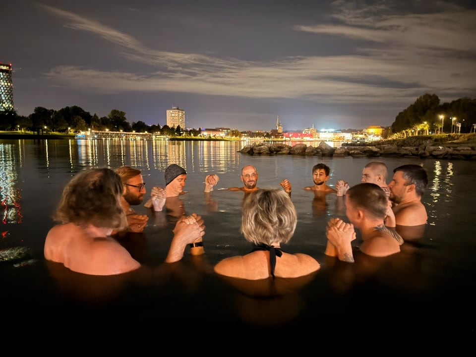Gruppe steht gemeinsam im nächtlichen Wasser an der Donau in Linz
