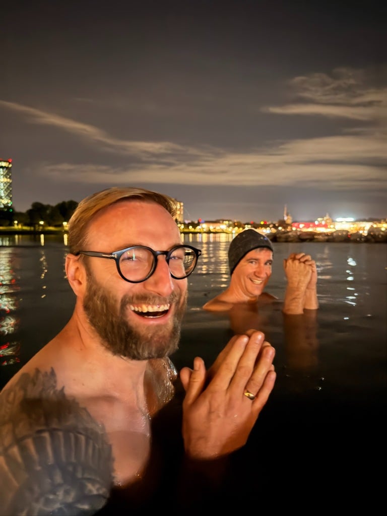 Teilnehmer lachen gemeinsam im Wasser vor der Linzer Stadtkulisse