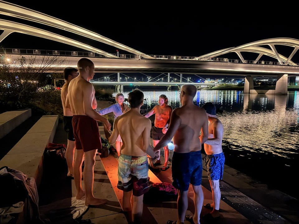 Eisbadegruppe steht unter der beleuchteten Eisenbahnbrücke in Linz