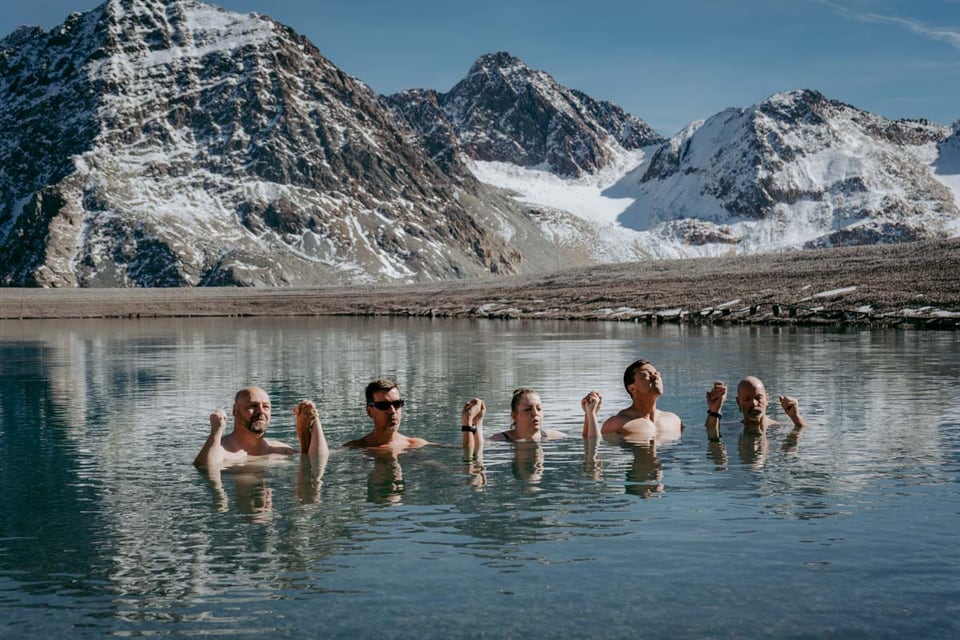 Retreatgruppe badet in einem klaren Bergsee vor schneebedeckten Gipfeln